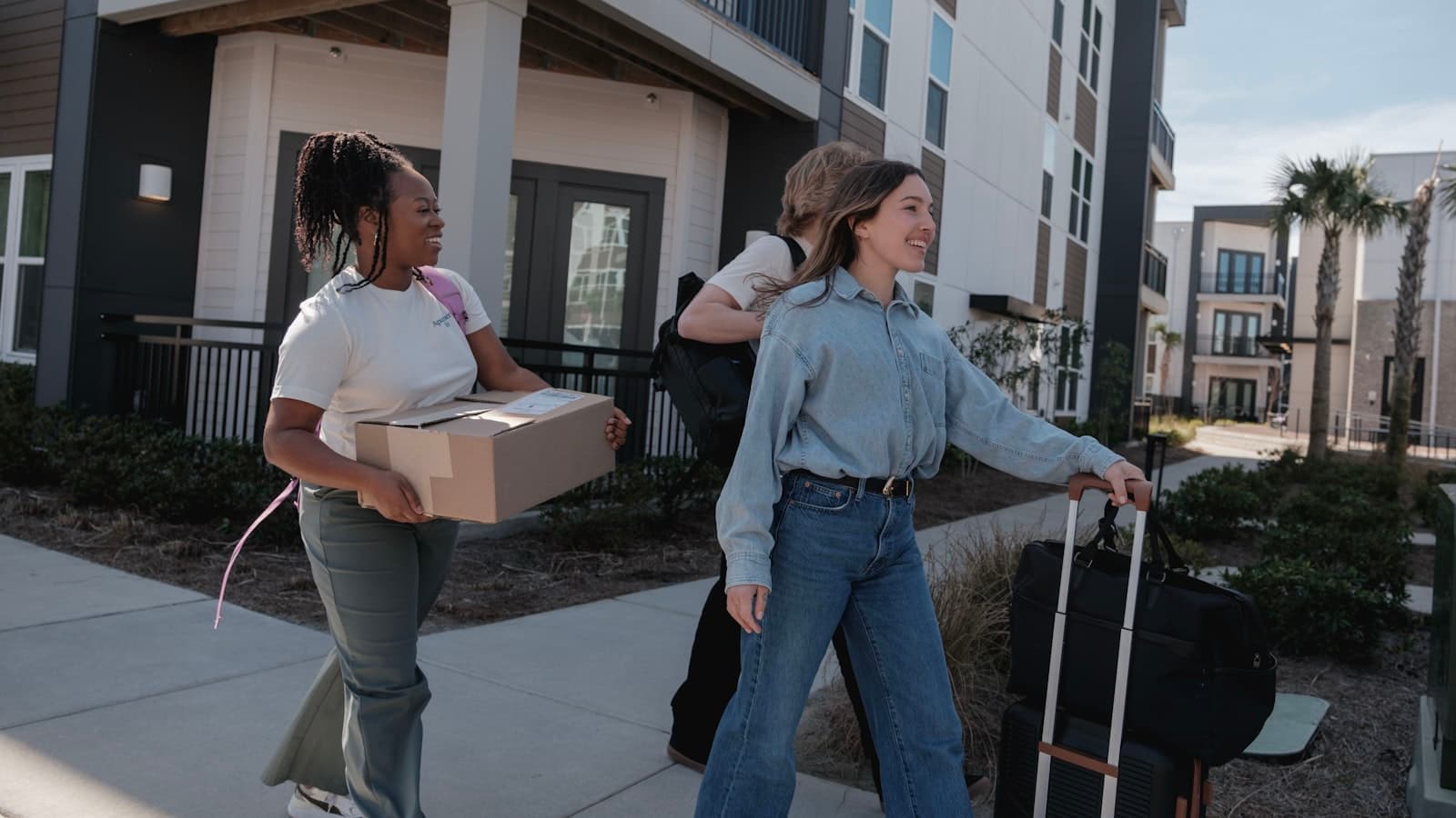 Jeunes alternants portant des cartons et des valises devant l'entrée de leur nouveau logement
