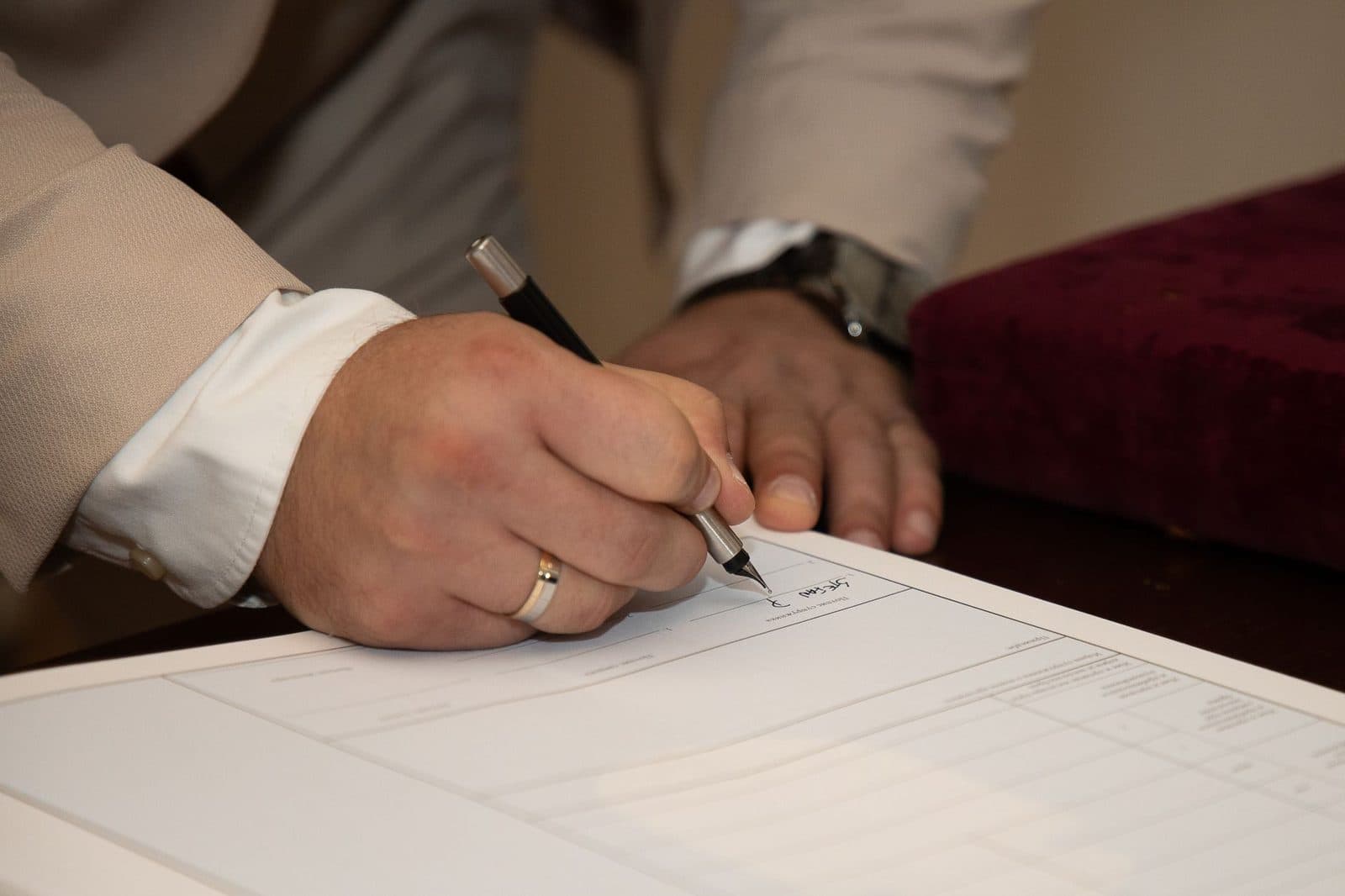 Gros plan sur la main d'un homme en chemise signant un document administratif avec un stylo