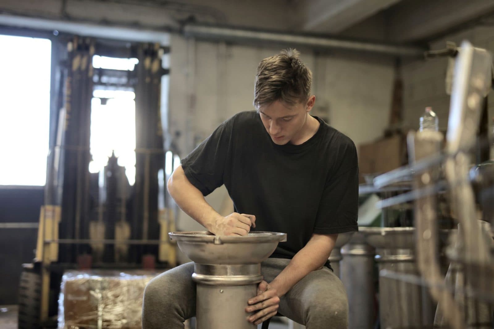 Jeune homme en t-shirt noir travaillant une pièce métallique dans un atelier industriel