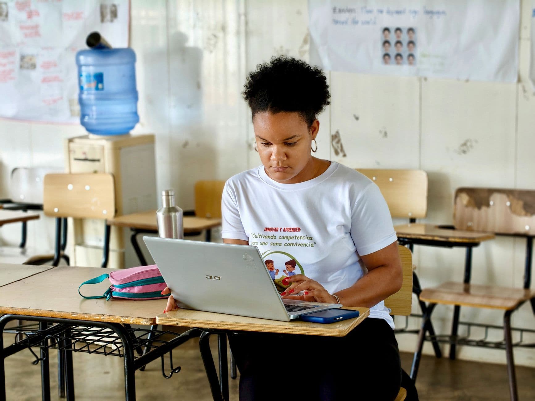 Une femme avec des cheveux crépus utilise un ordinateur portable portable assise à un bureau dans une salle de classe.