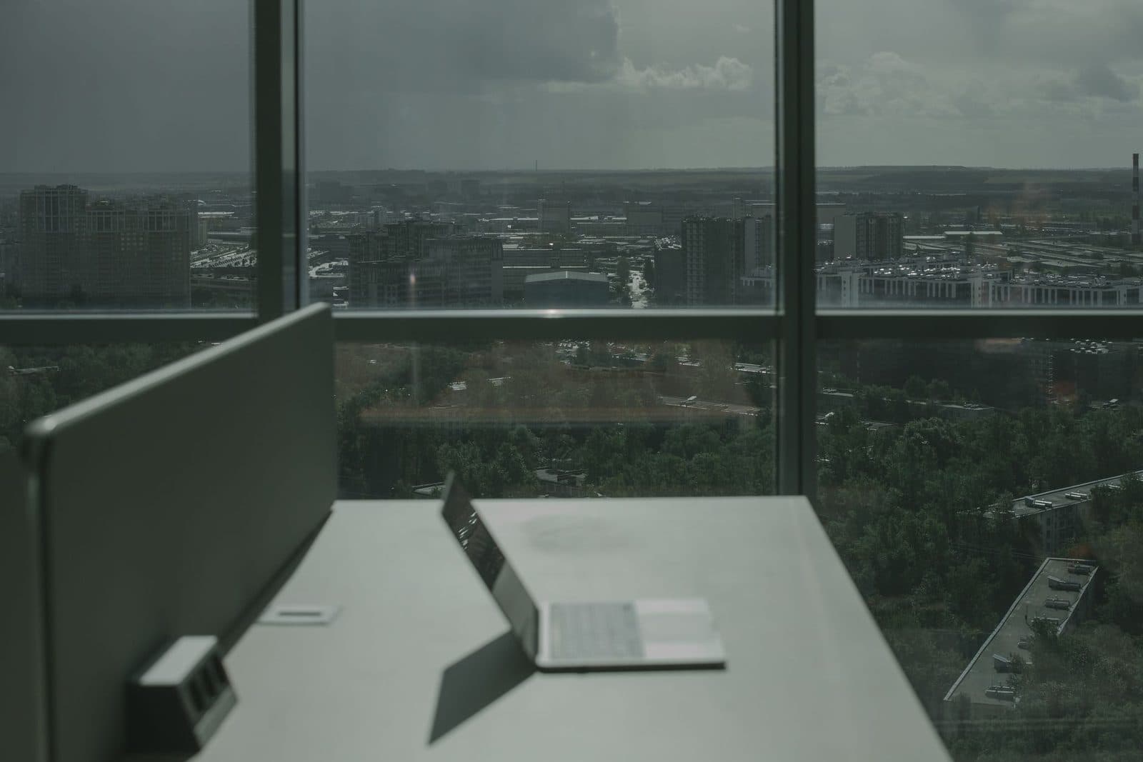 Un ordinateur portable ouvert sur un bureau face à une grande fenêtre avec vue sur une ville.