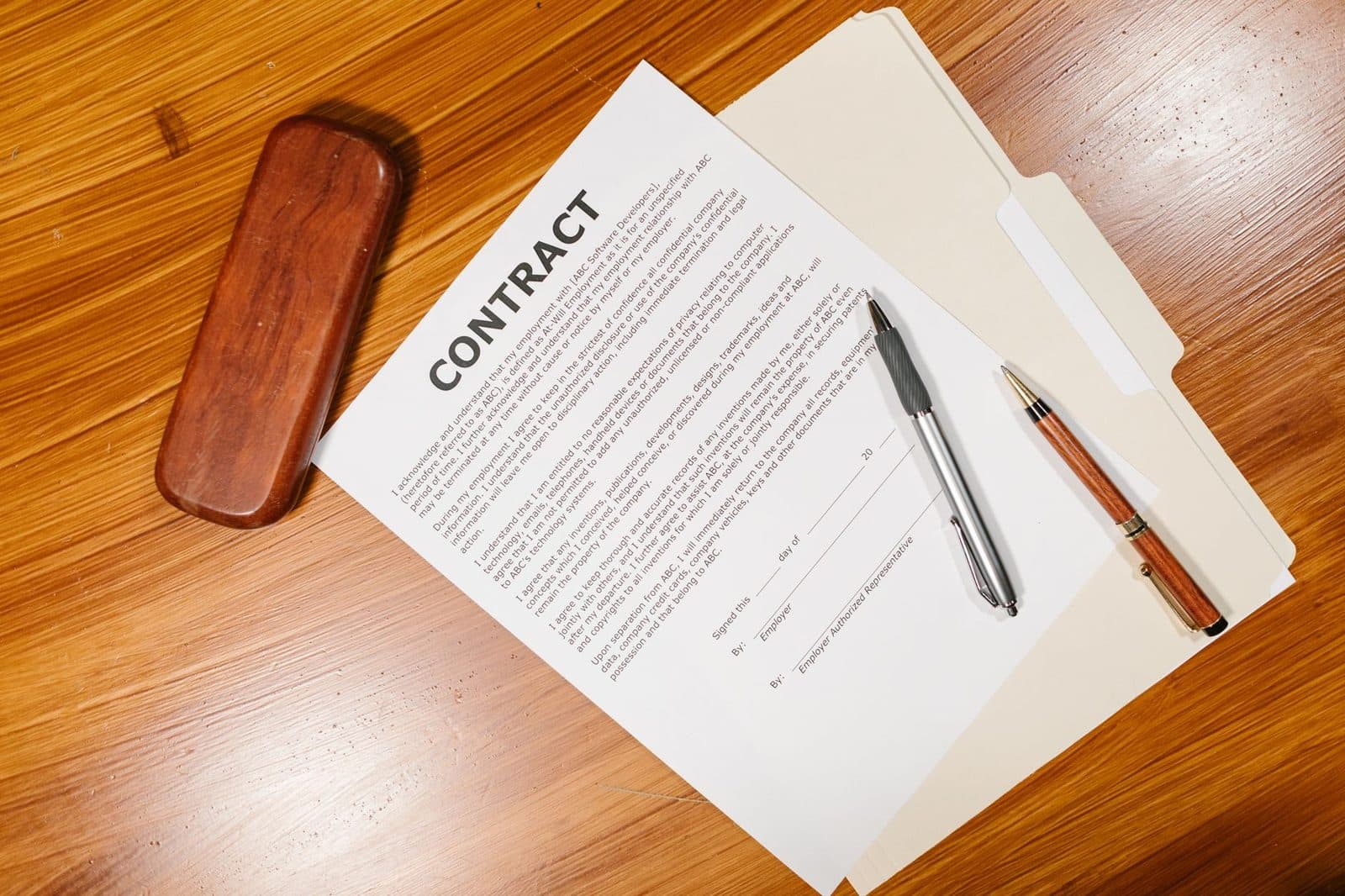 Contrat de travail en anglais posé sur une chemise cartonnée avec deux stylos, sur un bureau en bois