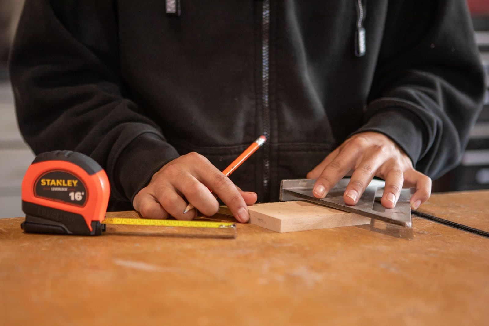Jeune homme traçant une planche de bois avec un crayon, une équerre et un mètre ruban sur un établi