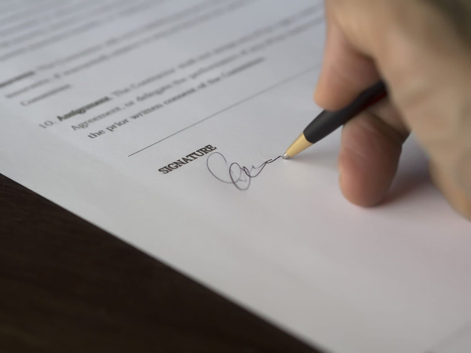 Main signant un contrat avec un stylo sur la ligne « signature » d'un document posé sur une table