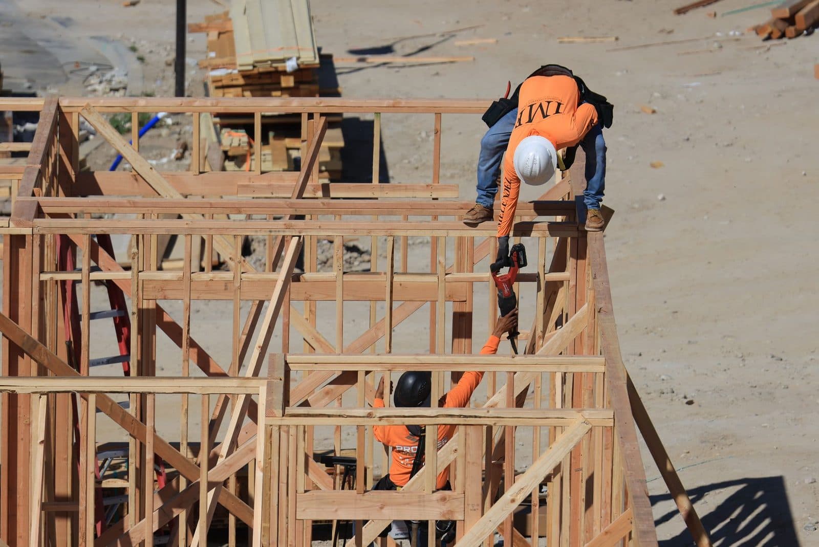 Two workers in orange gear and hard hats assembling a timber frame on a construction site