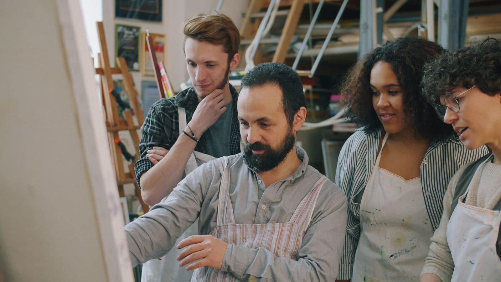 Formateur barbu en tablier montrant un travail à trois jeunes apprentis dans un atelier d'art