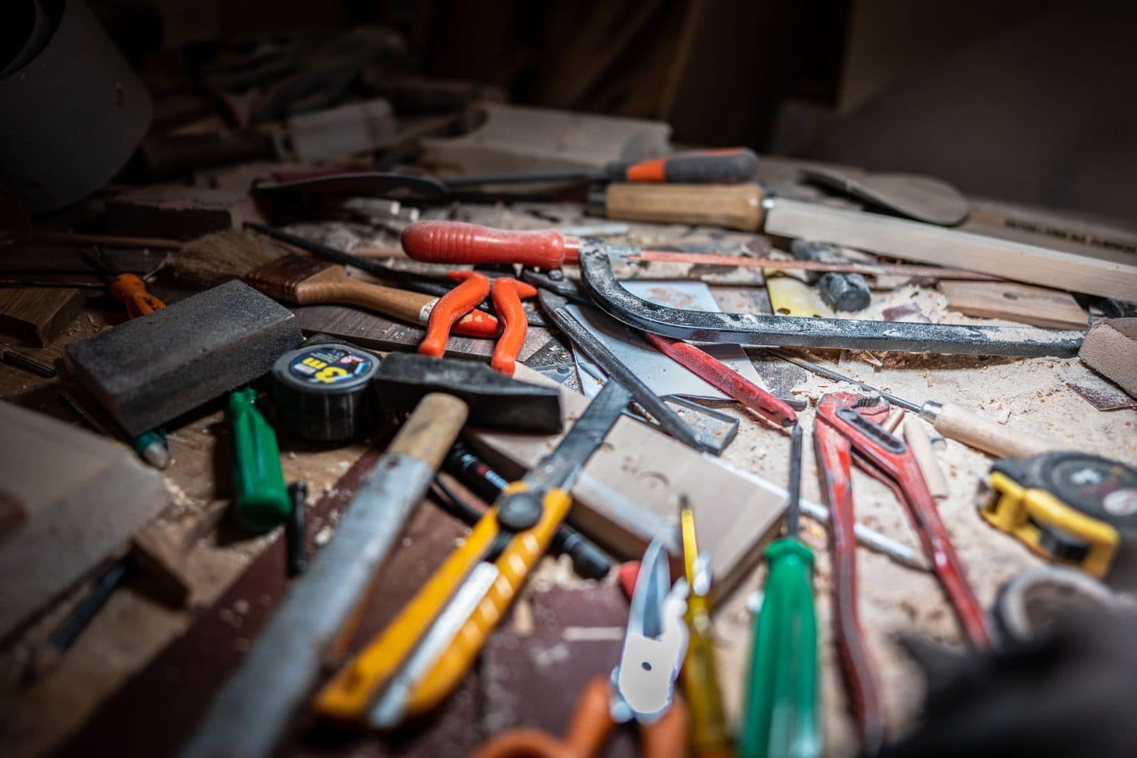 Outils de menuiserie éparpillés sur un établi couvert de sciure : scies, marteau, cutter, pinces et mètre ruban