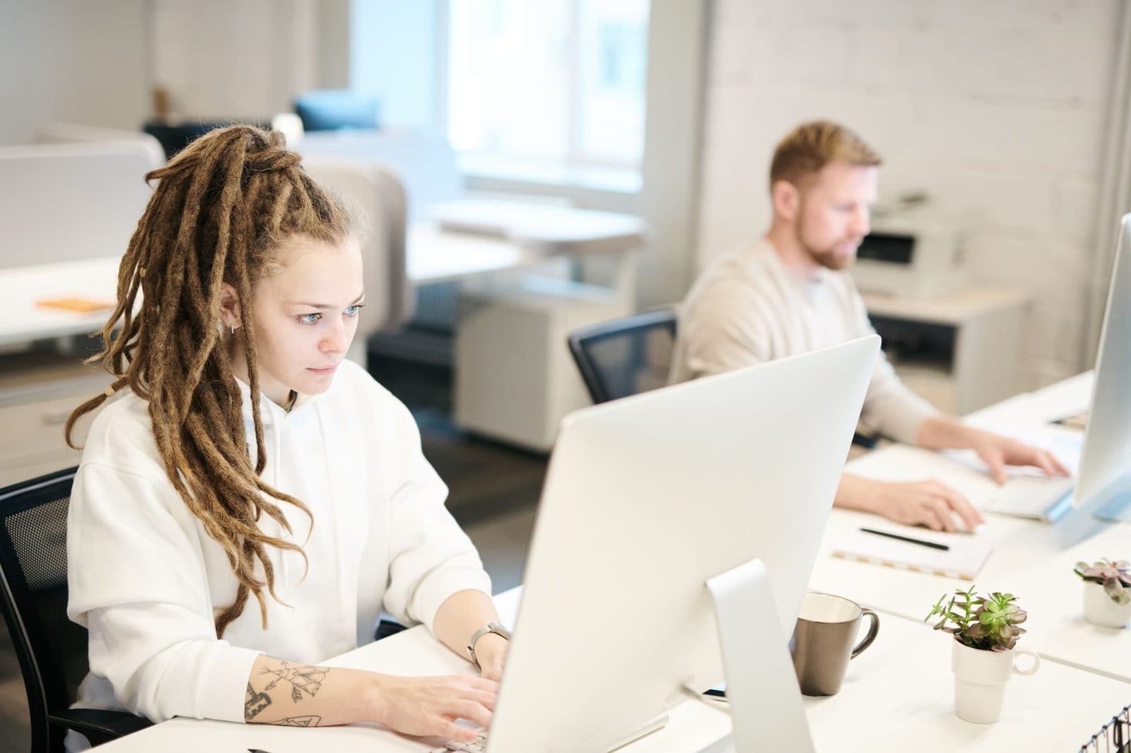 Jeune femme et homme travaillant sur ordinateur dans un bureau lumineux en open space