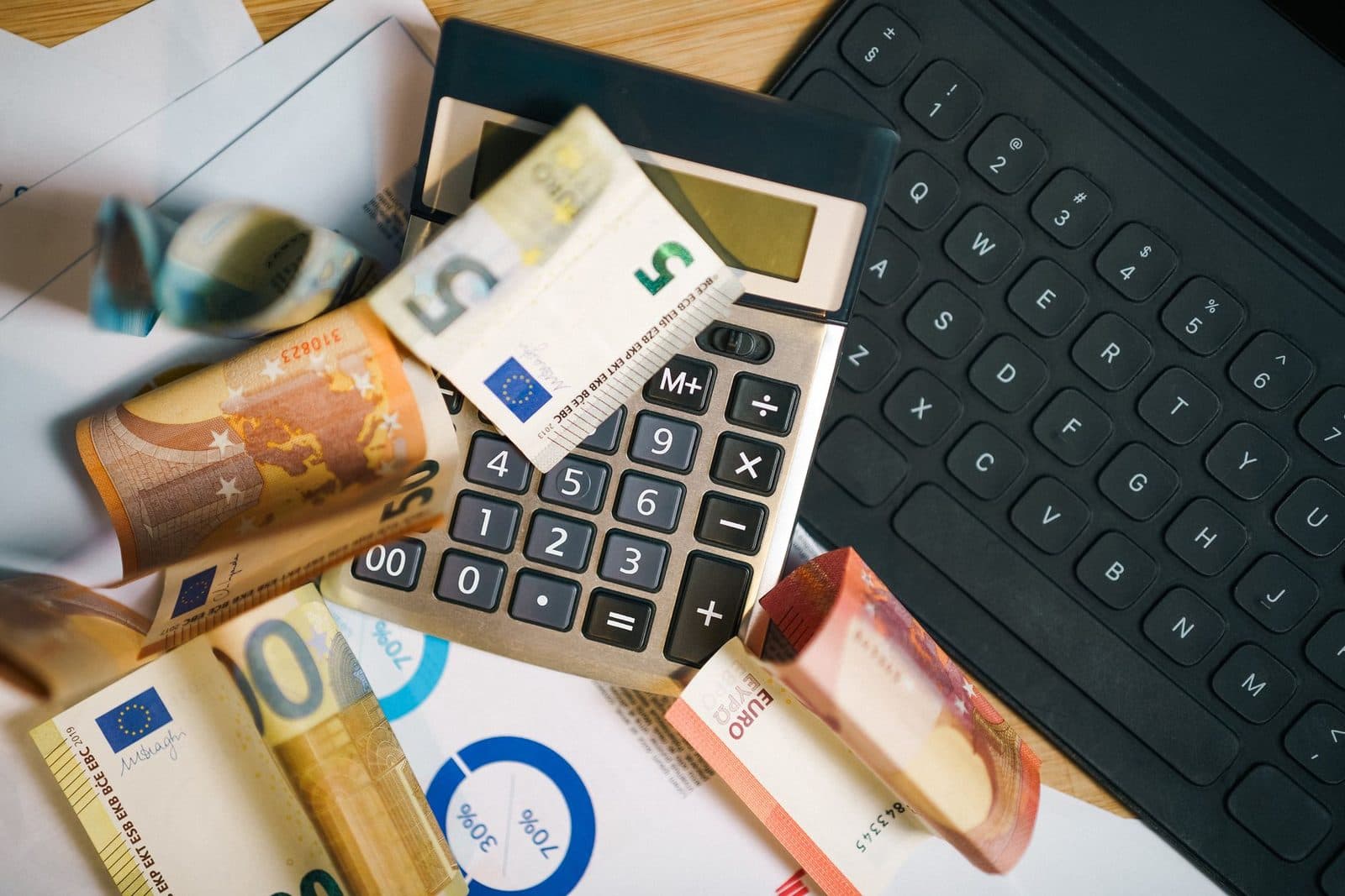 Billets en euros et calculatrice posés sur des documents près d'un clavier noir