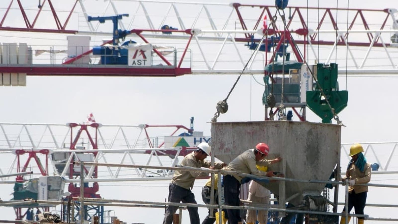 Ouvriers casqués guidant une benne à béton suspendue à une grue sur un chantier de construction