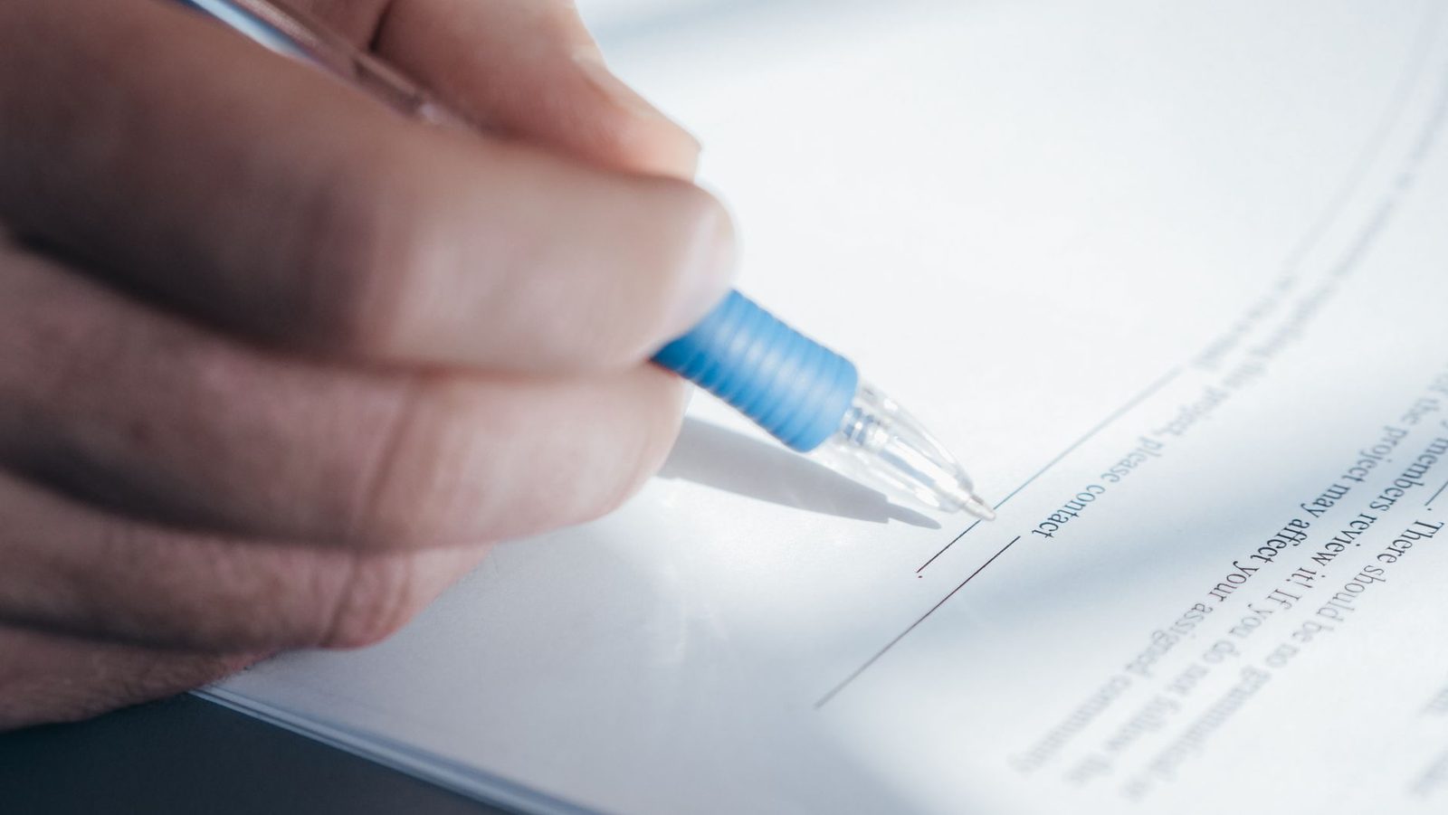 Main tenant un stylo bleu pour signer un document imprimé posé sur une table