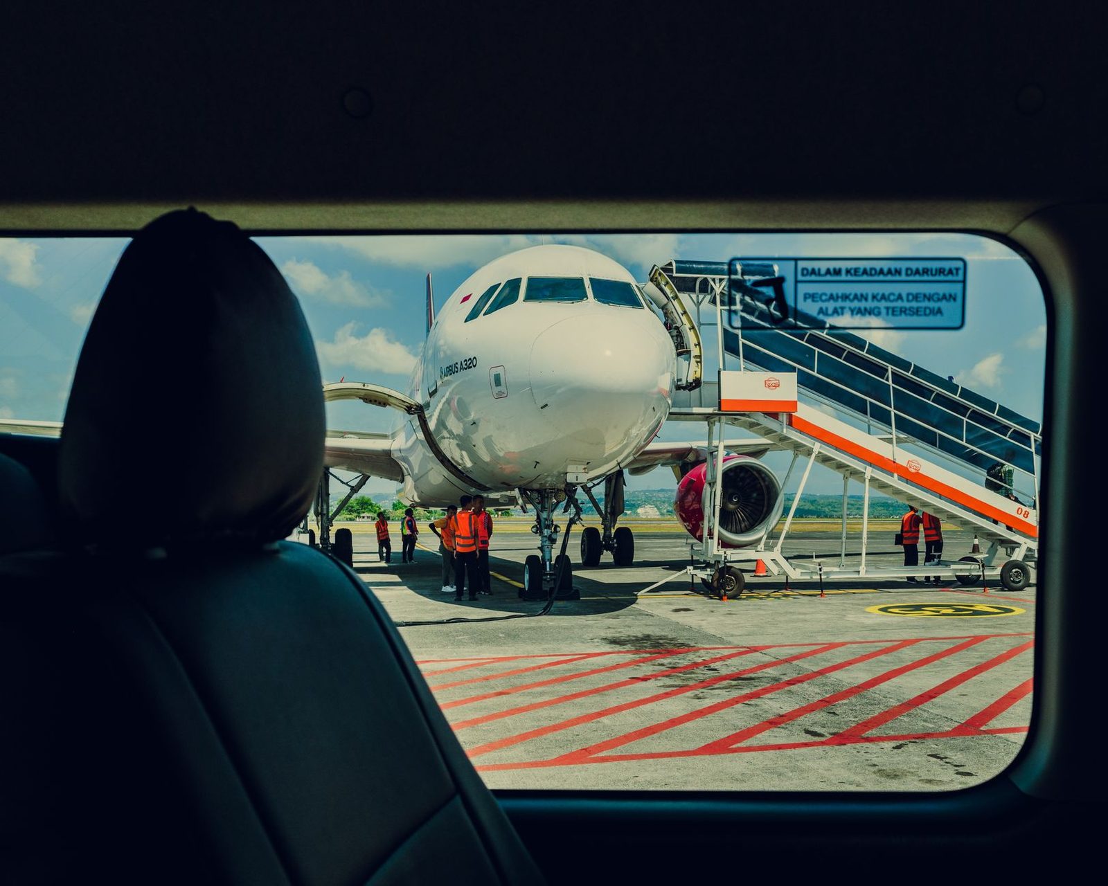 Avion Airbus A320 stationné sur le tarmac avec passerelle et personnel au sol en gilets orange, vu d'une vitre
