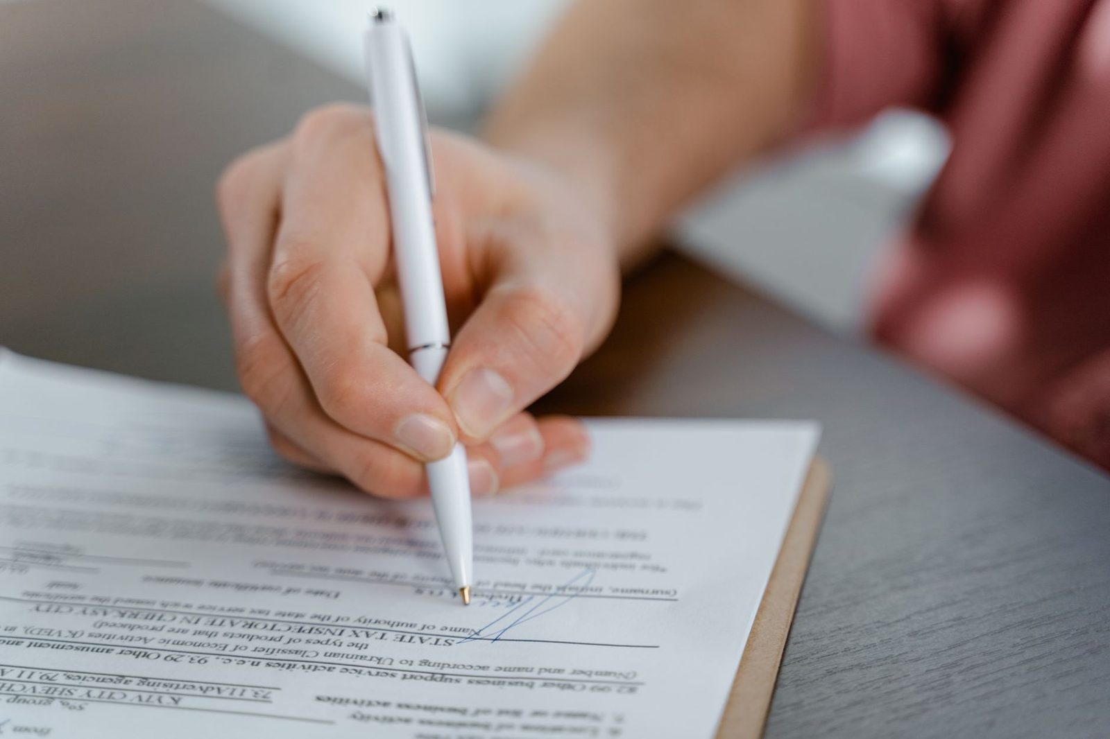 Gros plan sur une main tenant un stylo blanc et signant un document administratif posé sur un bureau