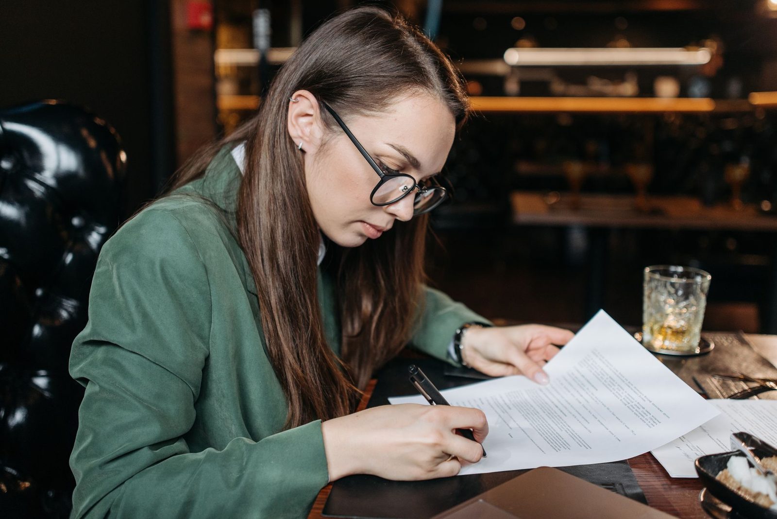 Jeune femme à lunettes signant un document sur une table en bois