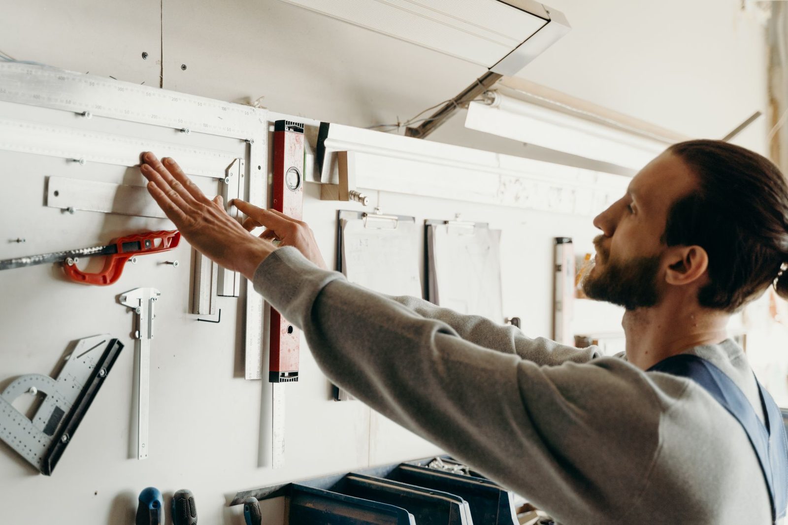 Jeune homme en atelier rangeant une règle et un niveau sur un panneau d'outils