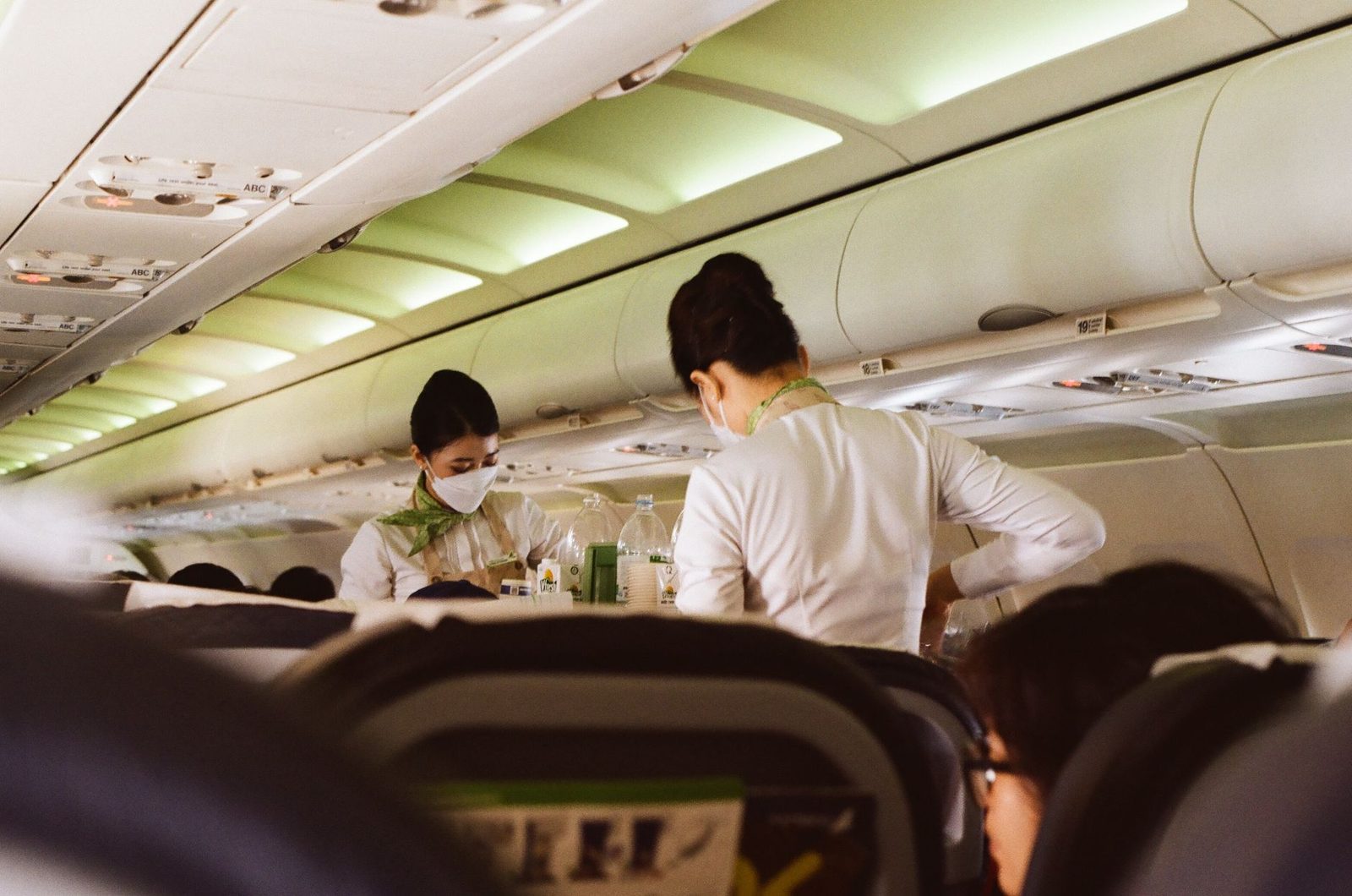Deux hôtesses de l'air masquées assurent le service en cabine d'un avion, entre les rangées de sièges