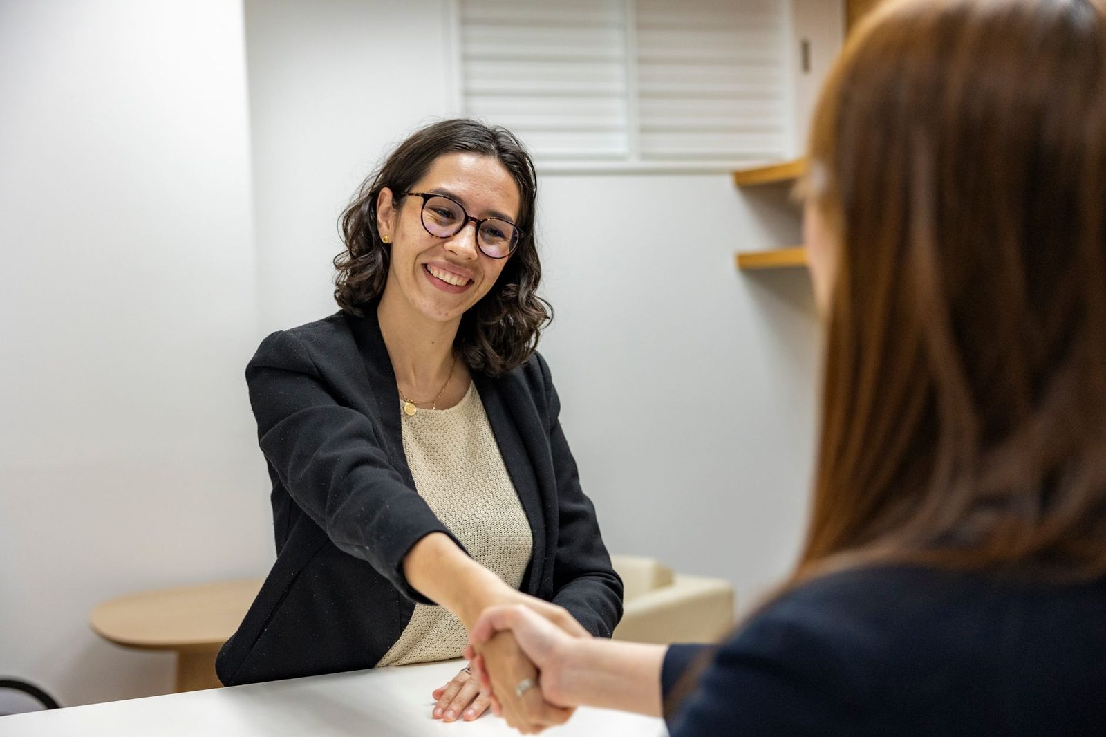 Jeune femme en veste noire souriante serrant la main d'une recruteuse lors d'un entretien d'embauche