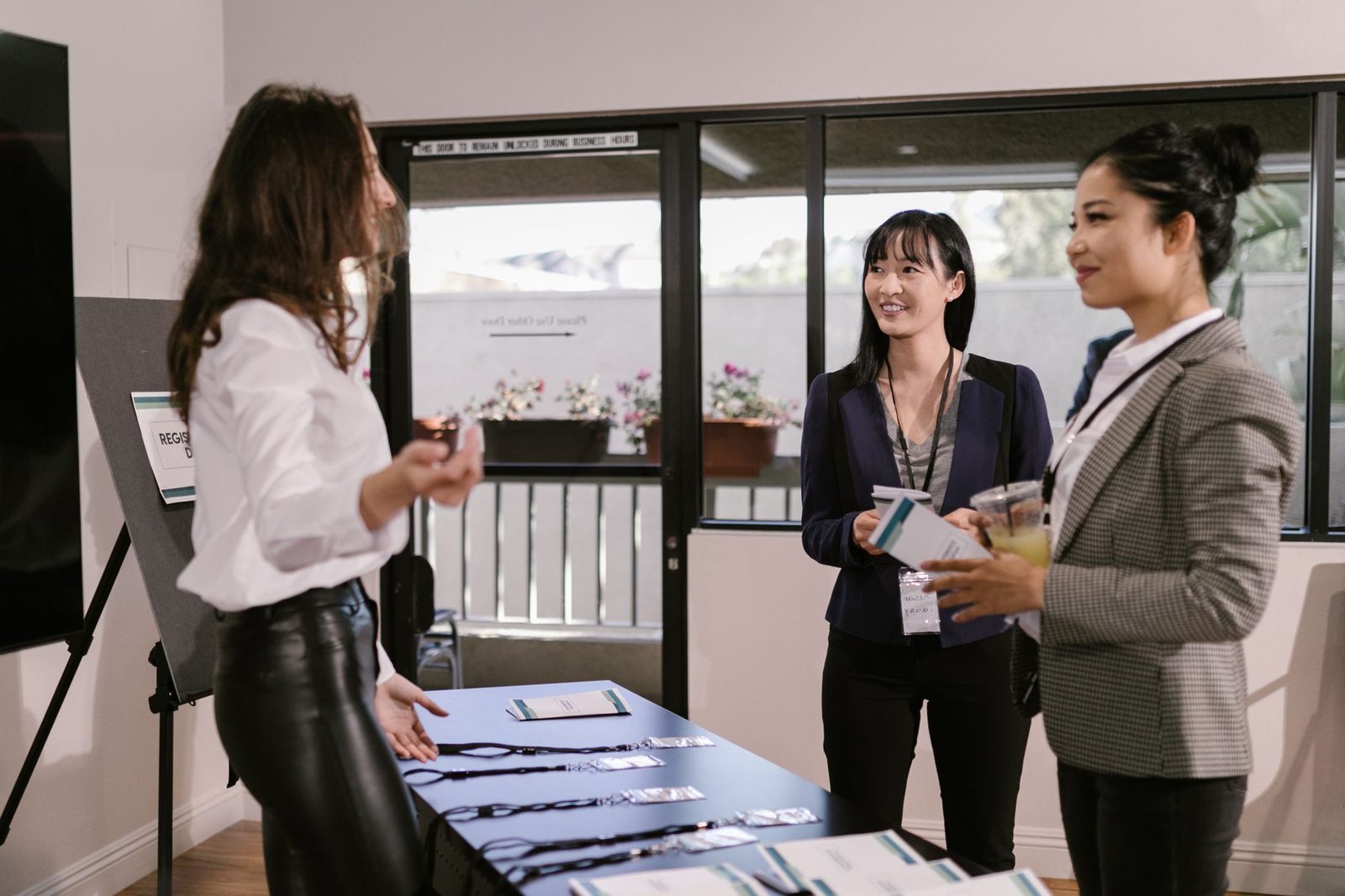 Trois jeunes femmes en tenue professionnelle discutent près d'une table d'accueil avec badges lors d'un événement