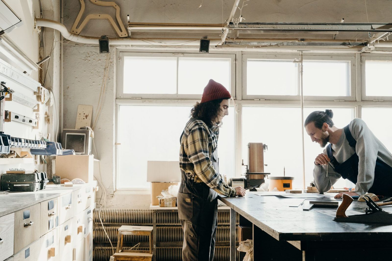 Deux artisans en salopette travaillent ensemble sur un établi dans un atelier lumineux