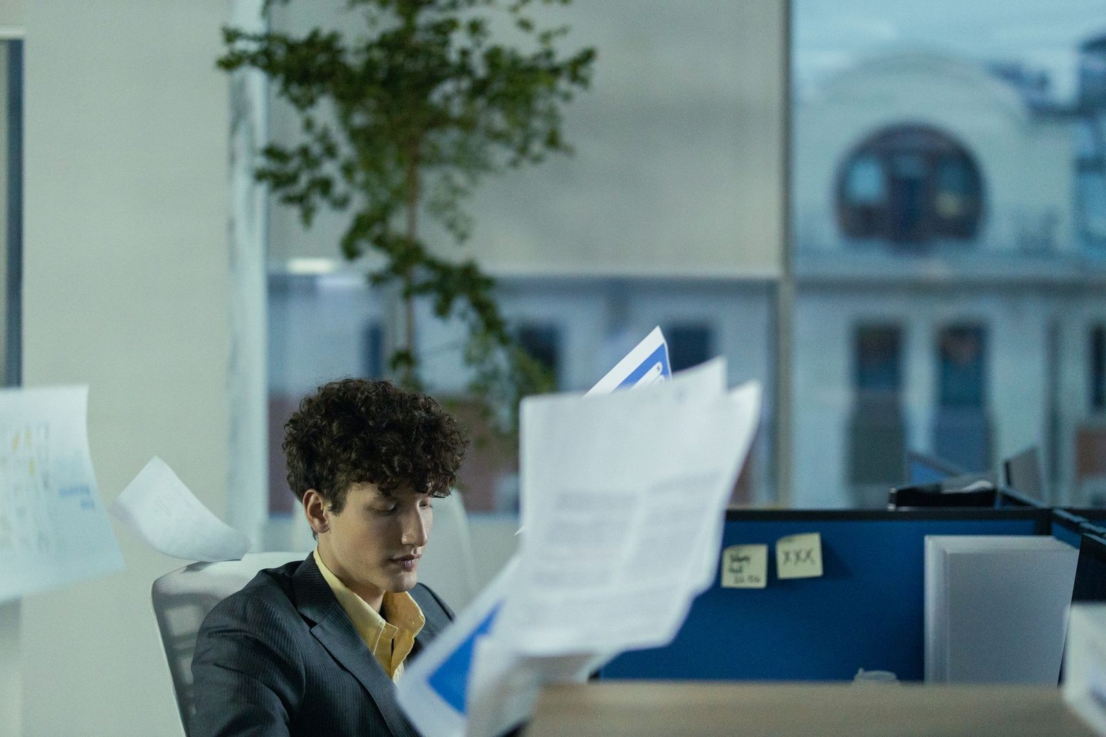 Jeune homme en costume assis dans un bureau, lisant des documents papier