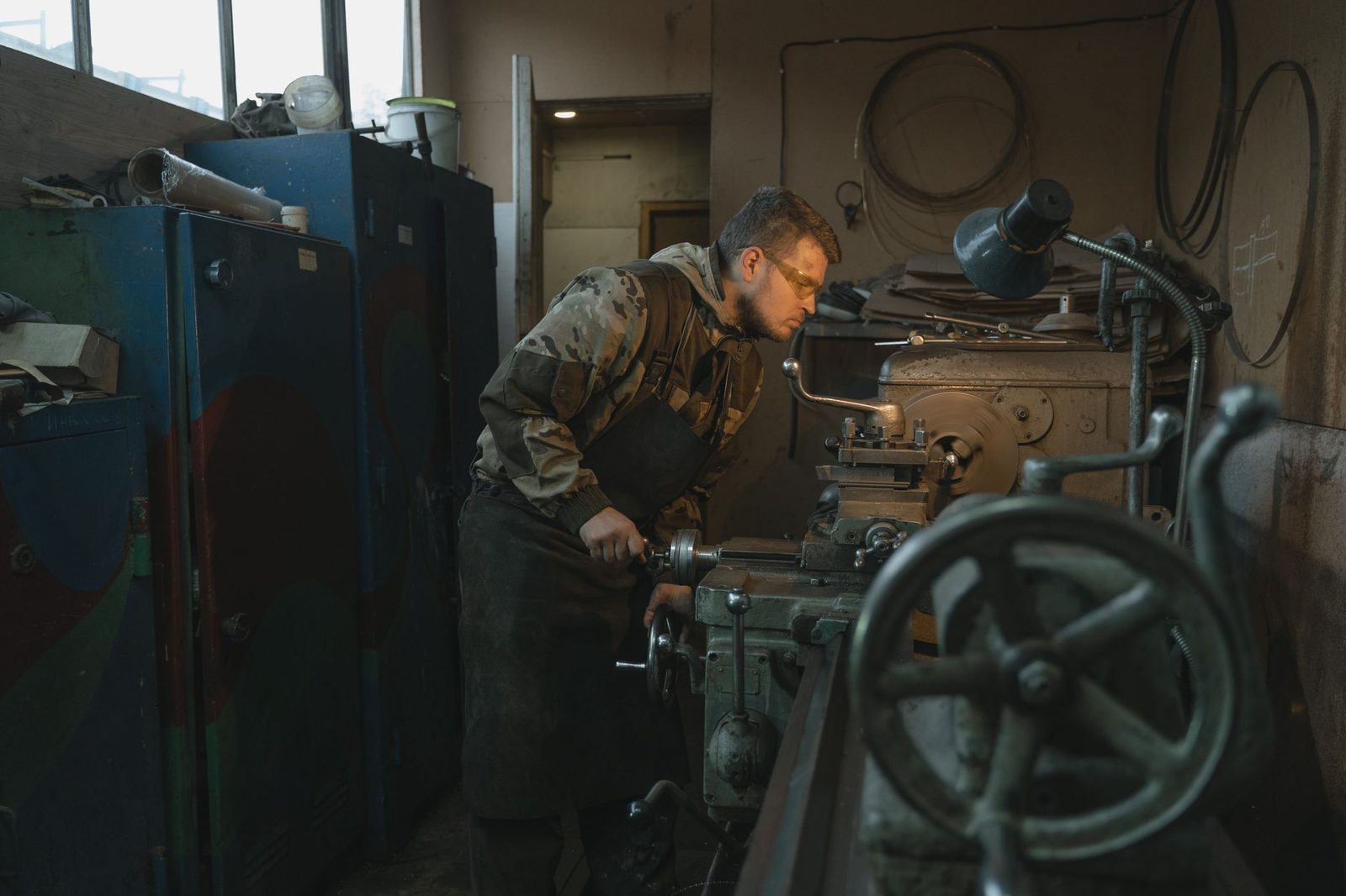 Jeune homme en tablier de cuir et lunettes de protection travaillant sur un tour dans un atelier