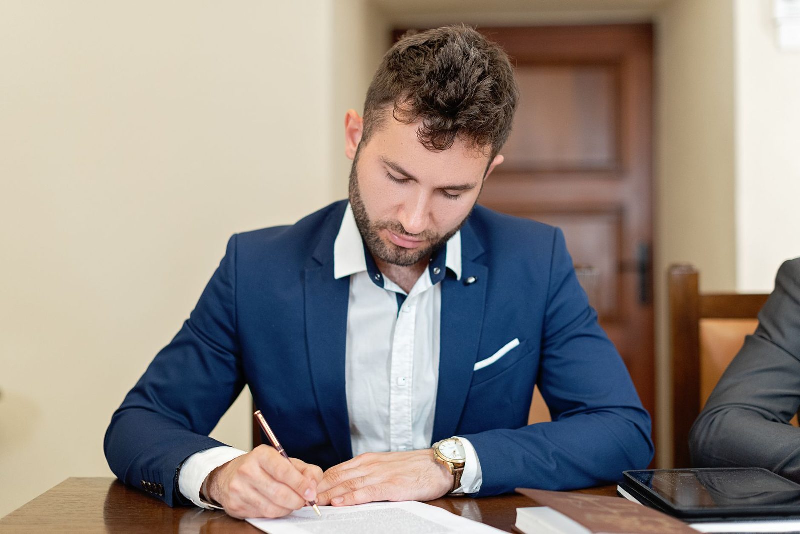 Jeune homme en costume bleu signant un document sur une table en bois dans un bureau