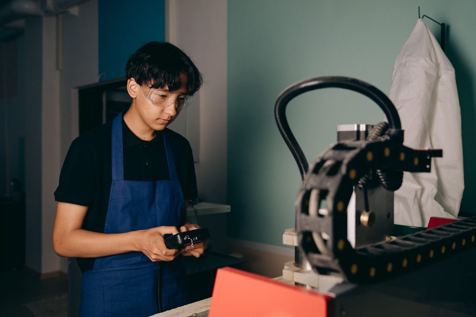 Jeune homme en tablier bleu et lunettes de protection utilisant une machine dans un atelier