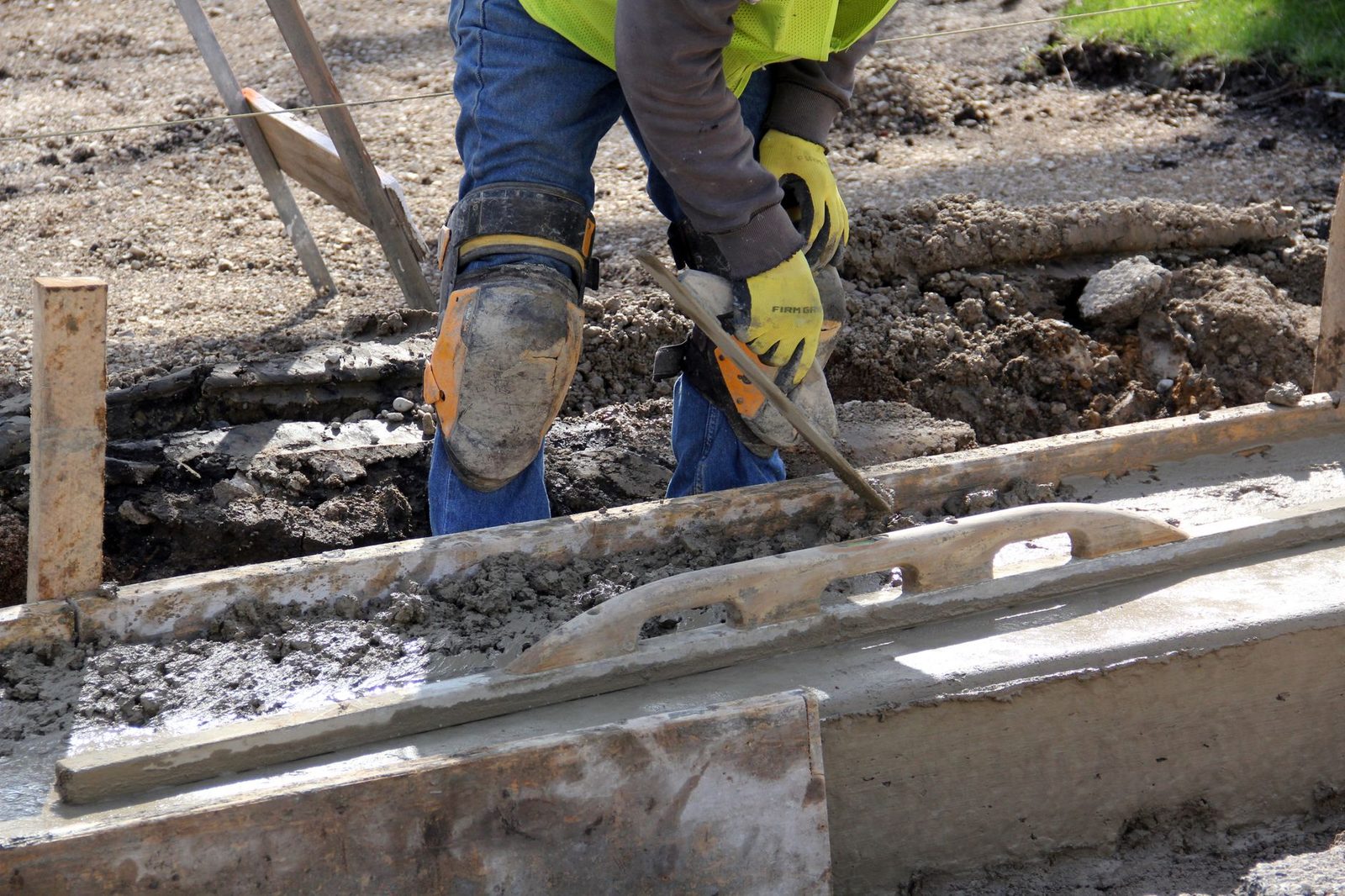 Ouvrier du bâtiment avec gants et genouillères lissant du béton frais sur un chantier