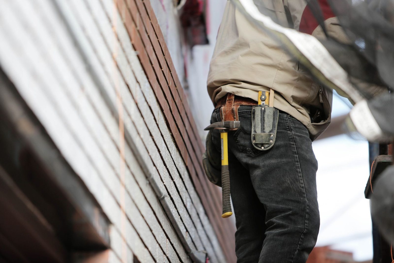 Ouvrier du bâtiment de dos avec marteau et porte-outils à la ceinture devant une façade