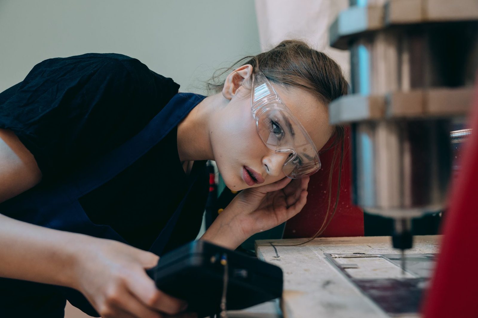 Jeune femme portant des lunettes de protection, penchée sur une machine dans un atelier
