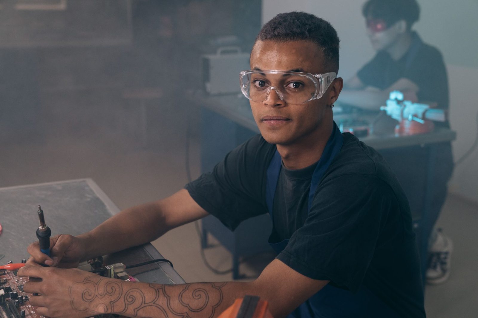 Jeune homme en lunettes de protection travaillant avec un fer à souder dans un atelier de formation
