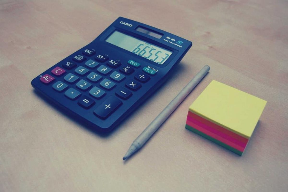 Un carnet ouvert sur un tableau de dépenses mensuelles, à côté d'une calculatrice et d'une tasse de café