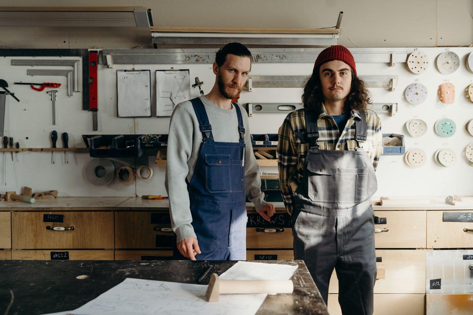 Deux jeunes hommes en salopette de travail debout dans un atelier de menuiserie équipé d'outils