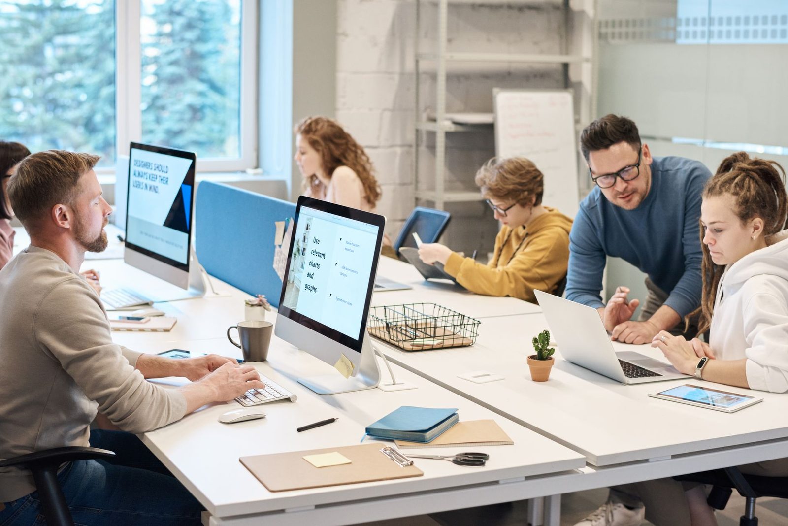 Jeunes salariés travaillant sur ordinateurs dans un bureau open space, un collègue les accompagne