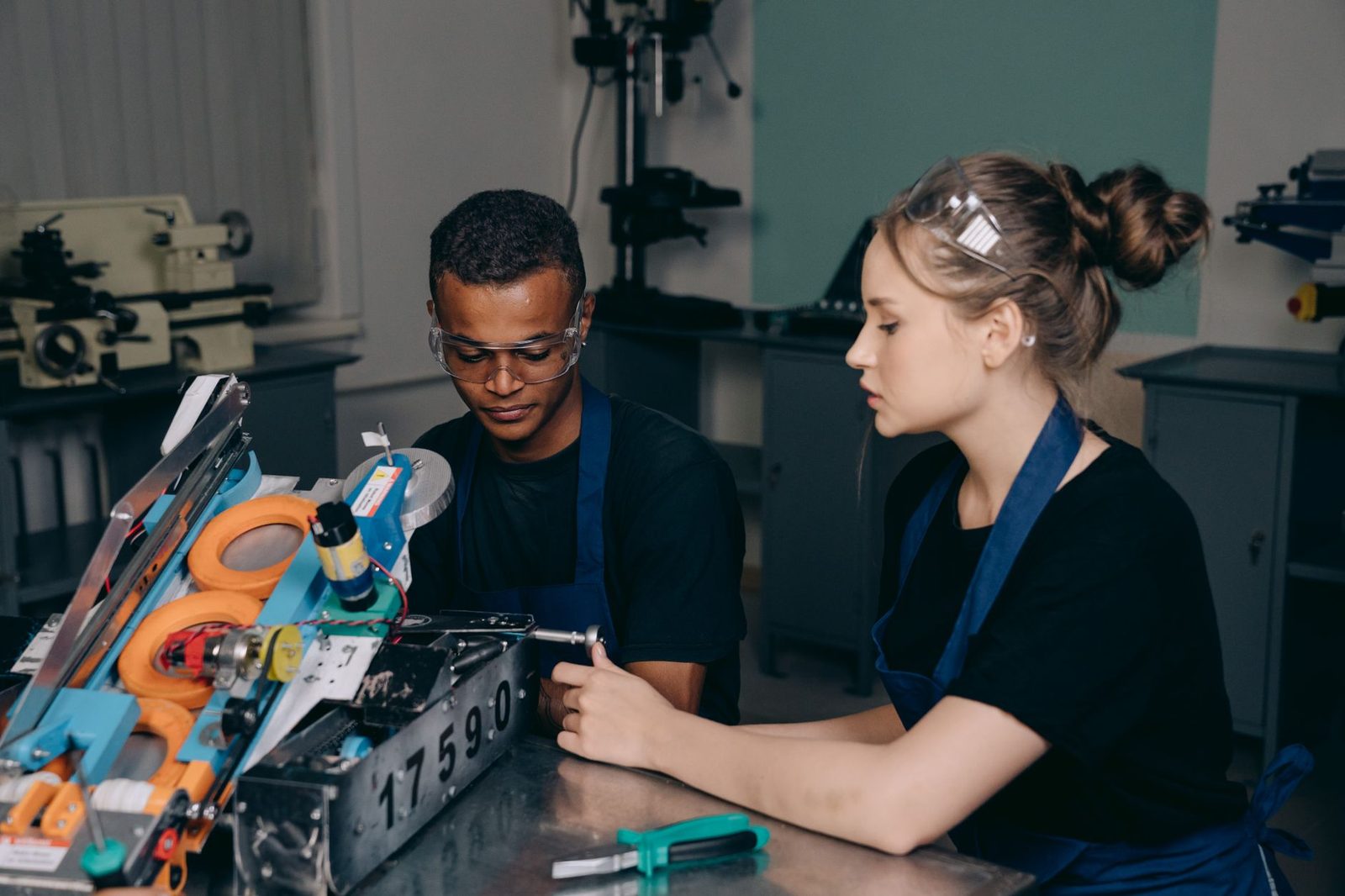 Deux jeunes apprentis en tablier et lunettes de protection travaillent sur une machine dans un atelier