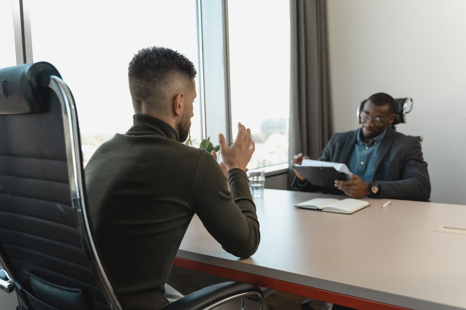 Deux hommes en entretien dans une salle de réunion, l'un consultant des documents face à un candidat