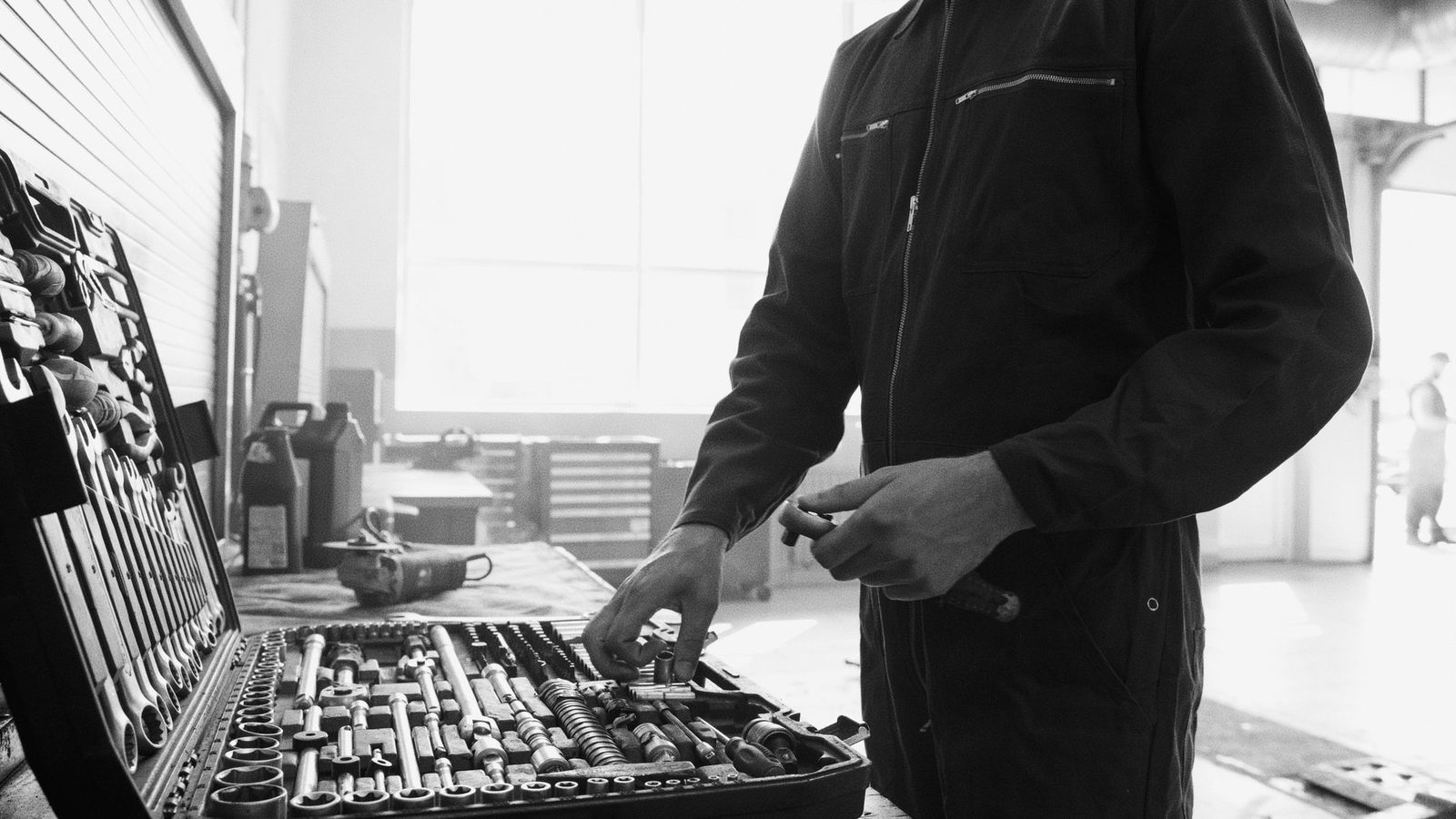 Technicien en combinaison de travail choisissant un outil dans une caisse à outils, en atelier