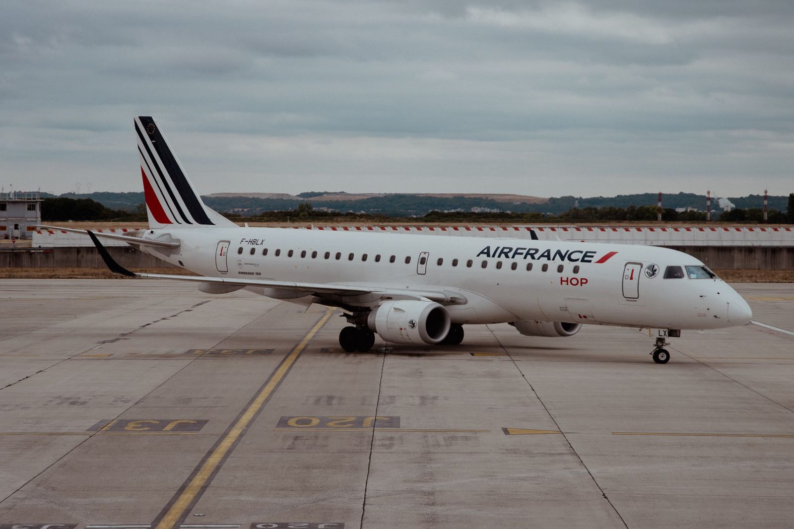 Avion Air France HOP Embraer 190 stationné sur le tarmac d'un aéroport sous un ciel nuageux