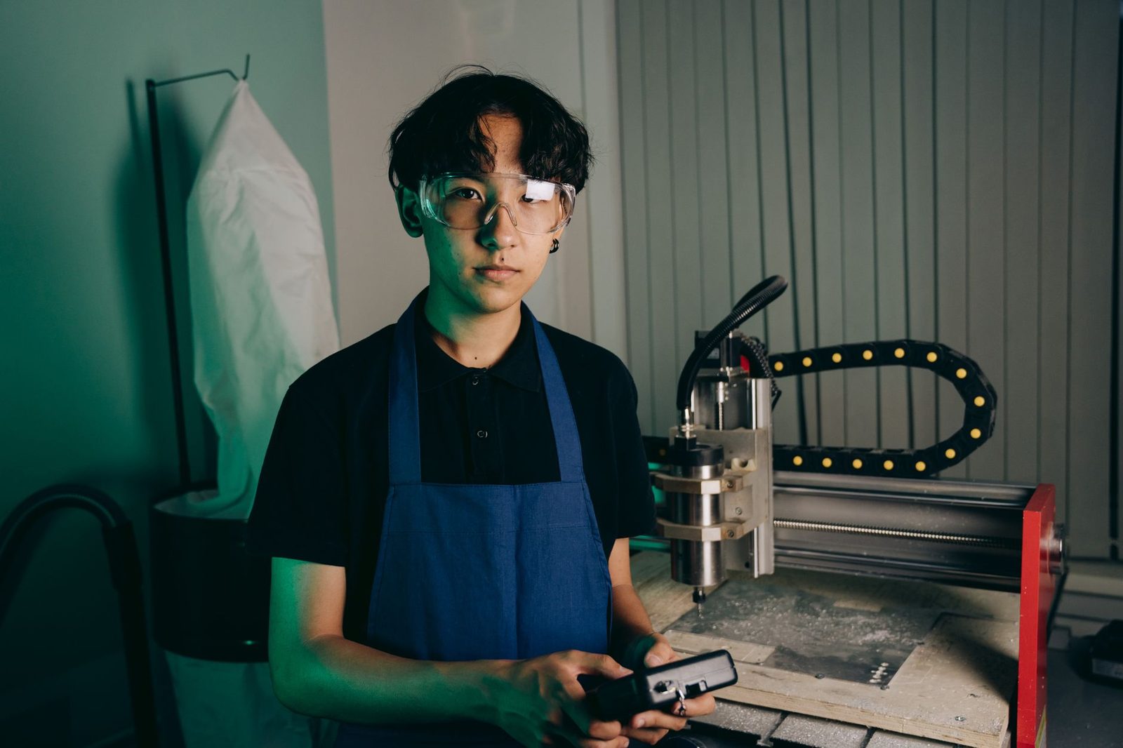 Jeune apprenti en tablier bleu et lunettes de protection devant une machine-outil dans un atelier