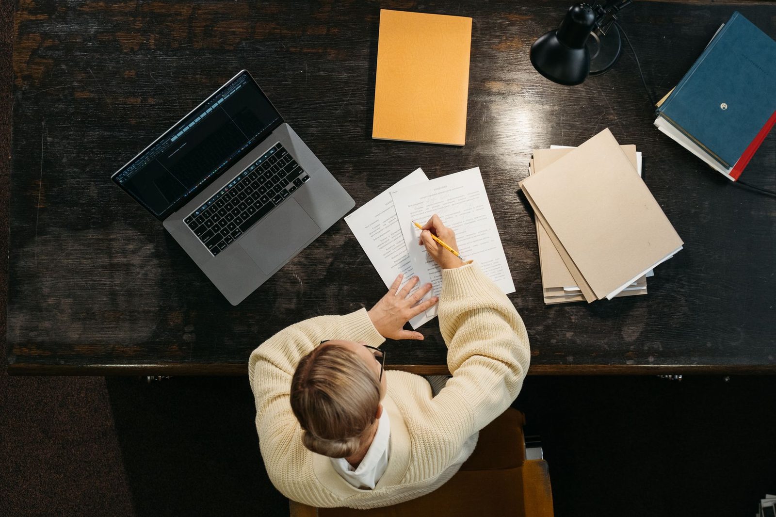 Vue de dessus d'une personne travaillant à un bureau avec un ordinateur portable, des cahiers et des documents.