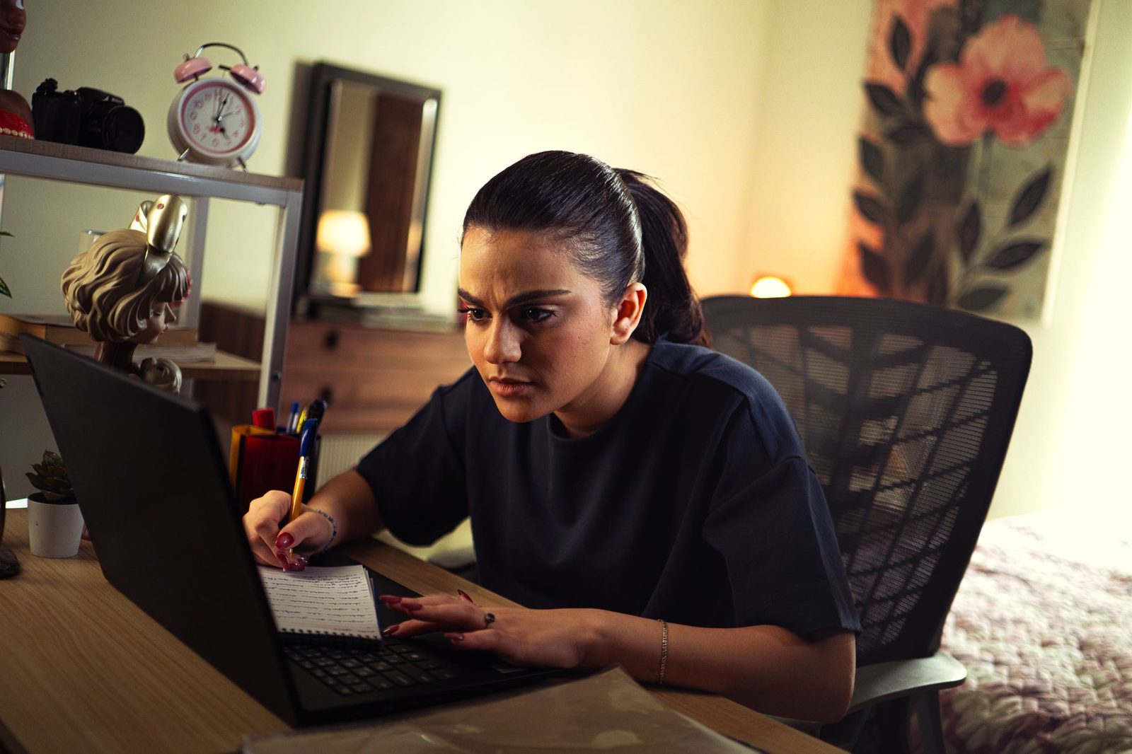 Une jeune femme concentrée travaillant sur un ordinateur portable et prenant des notes sur un bureau.
