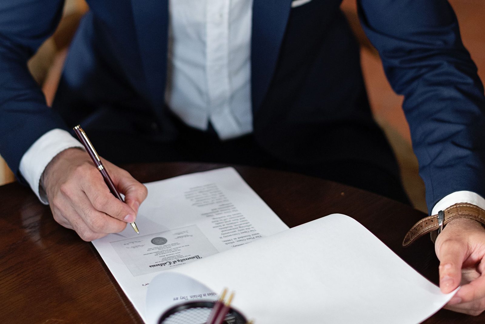 Homme en costume signant des documents avec un stylo sur une table en bois