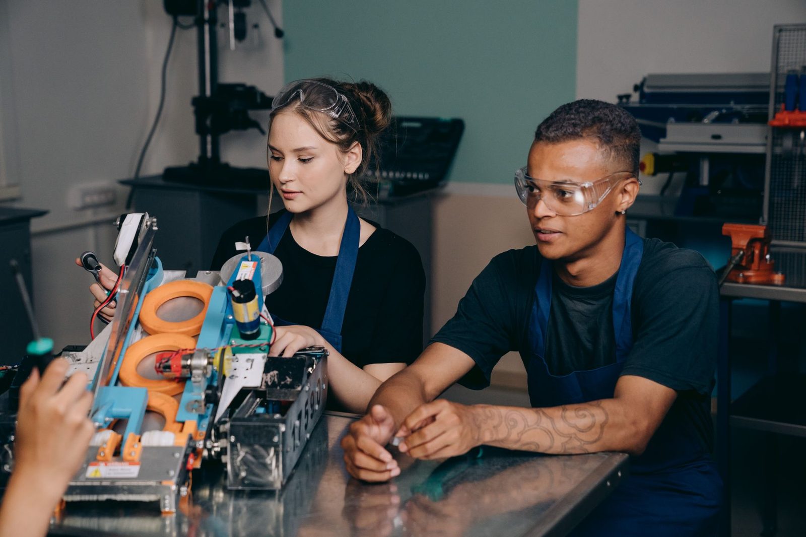 Deux jeunes en tablier et lunettes de protection travaillant sur une machine dans un atelier de formation