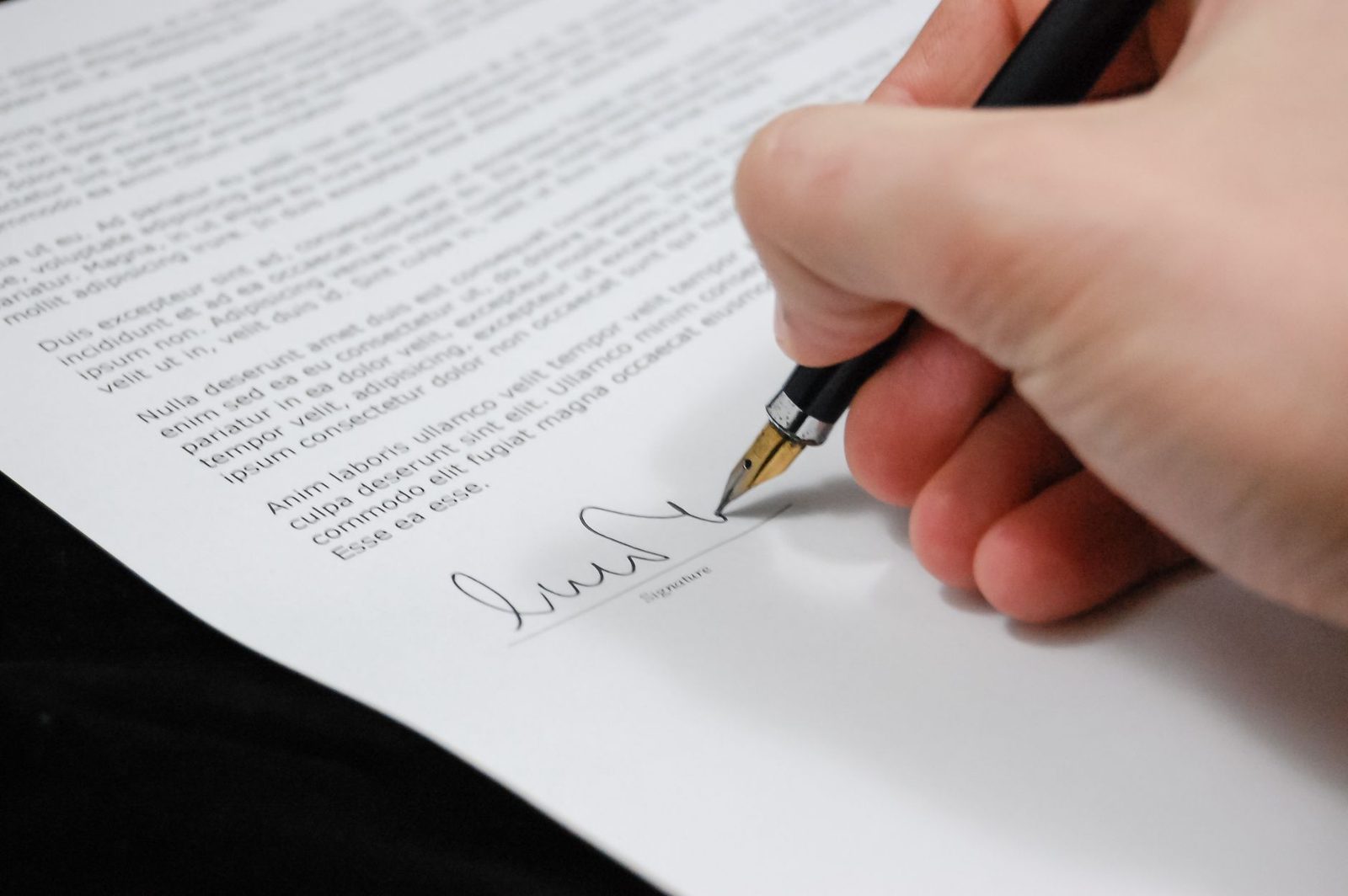 Main signant un contrat imprimé avec un stylo plume, gros plan sur la signature