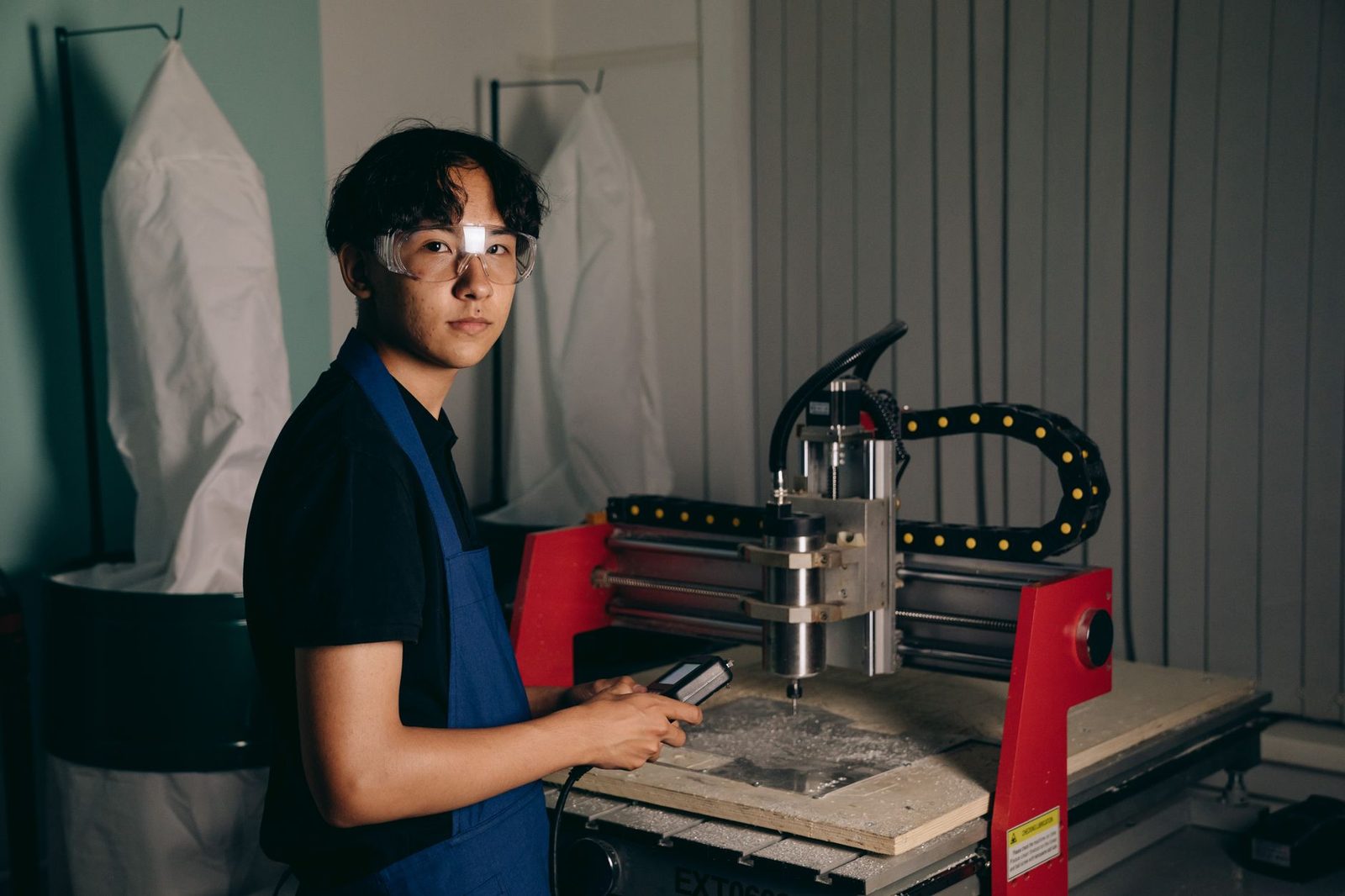 Jeune apprenti en tablier bleu et lunettes de protection utilisant une fraiseuse numérique dans un atelier