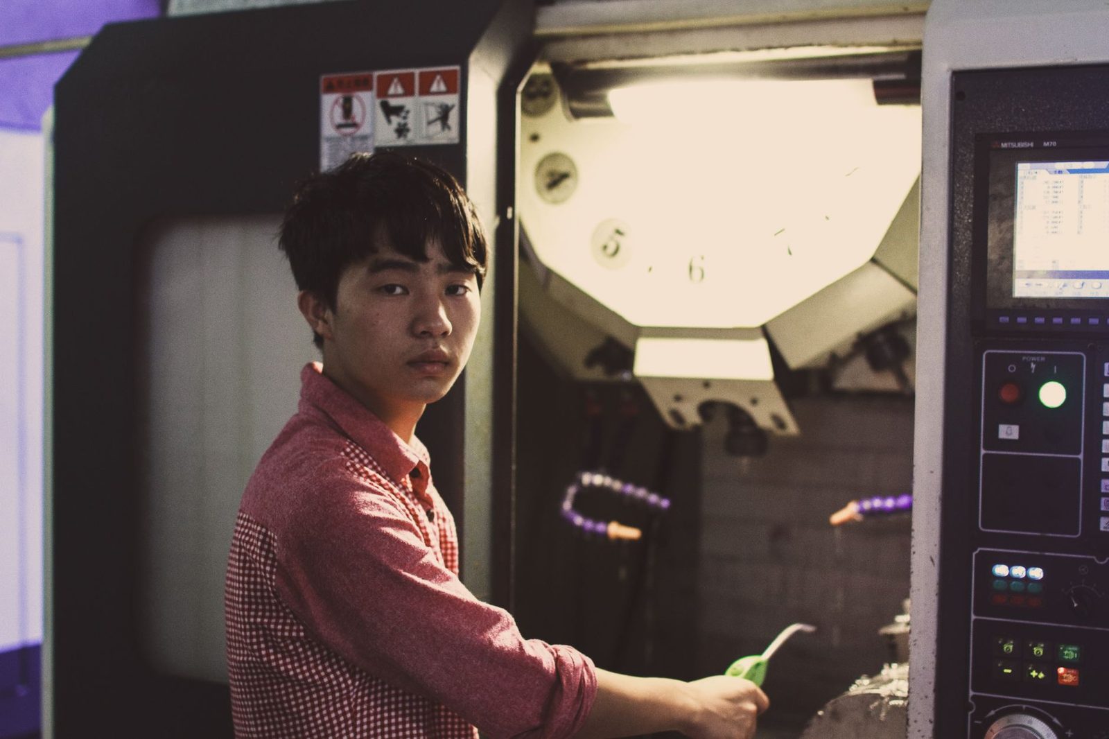 Jeune homme en chemise à carreaux utilisant une machine-outil à commande numérique dans un atelier