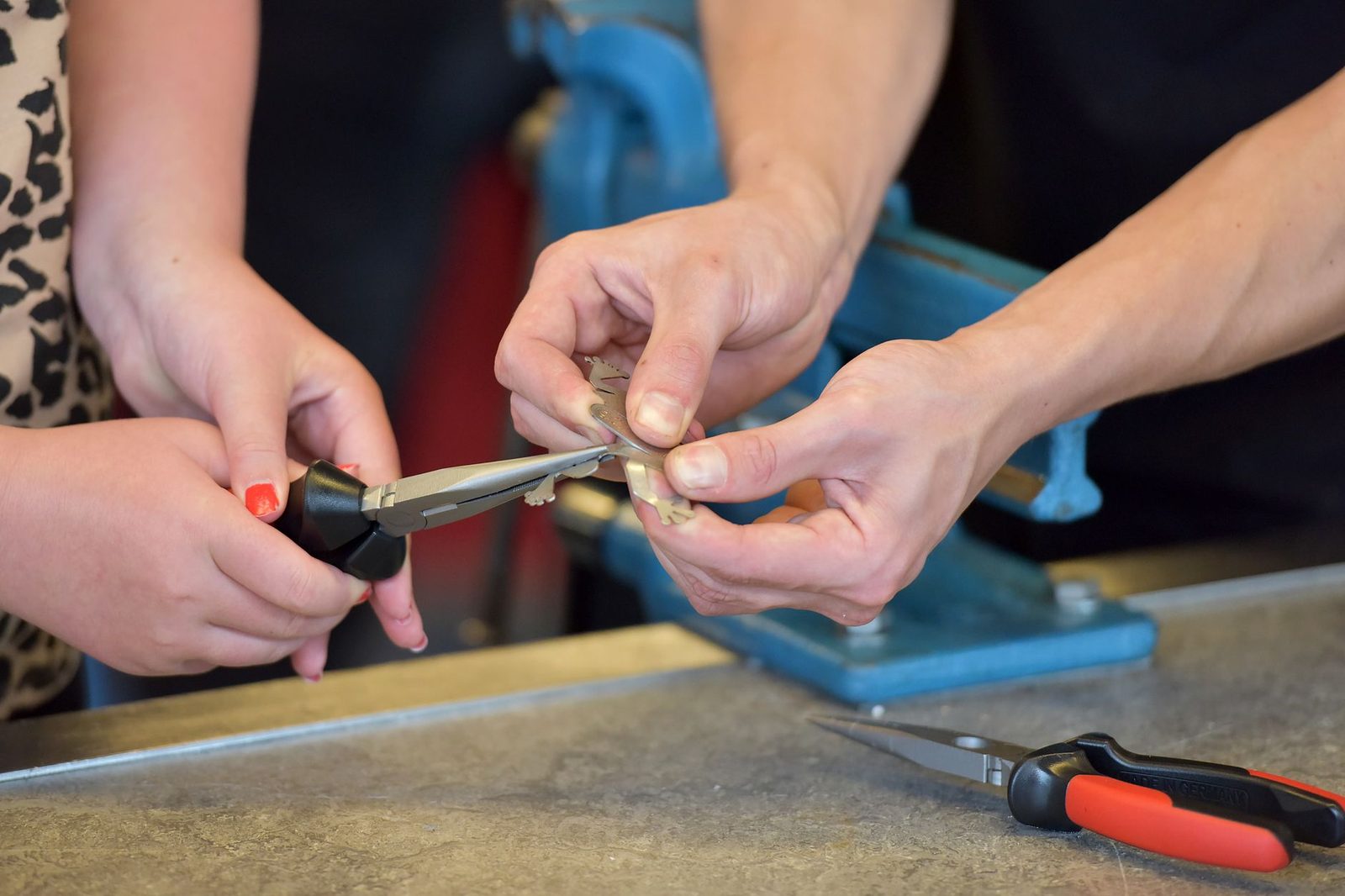 Mains d'un formateur guidant une apprentie manipulant une pince sur un établi d'atelier