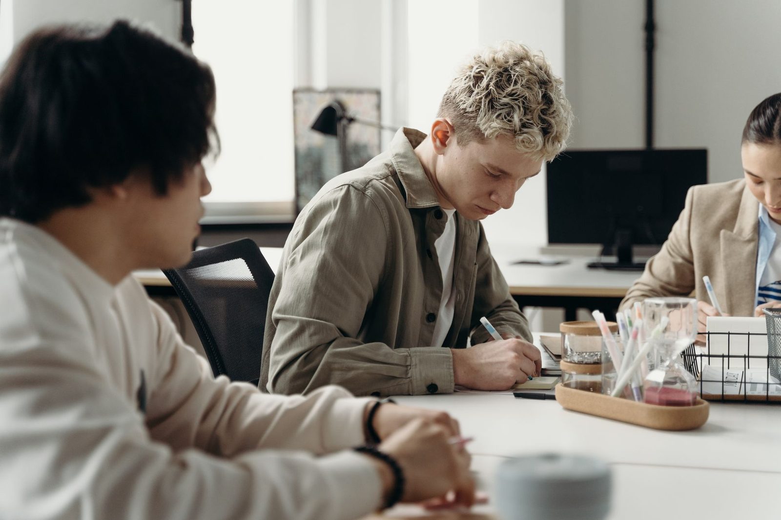 Trois jeunes salariés assis autour d'une table de bureau, prenant des notes pendant une réunion